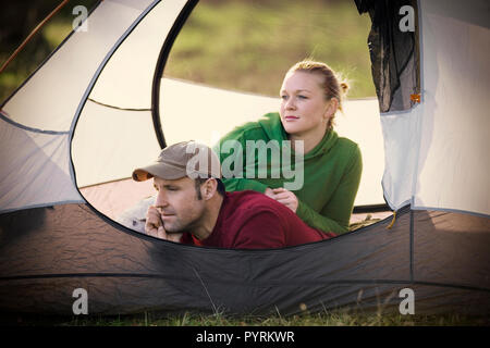 Junge erwachsene Paare liegen in einem Zelt in einem Feld. Stockfoto