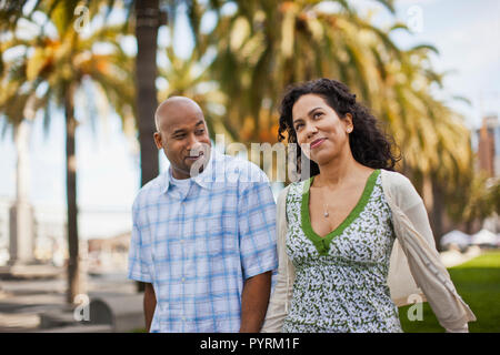 Mitte der erwachsenen Frau schaut nachdenklich, als sie Spaziergänge mit ihrem Ehemann durch einen Park in der Stadt. Stockfoto