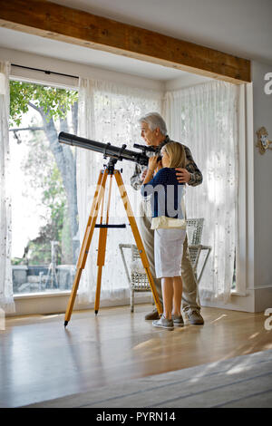 Älterer Mann seine junge Enkelin Unterstützung bei der Suche durch ein Teleskop. Stockfoto