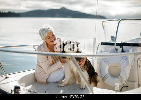 Lächelnd reife Frau entspannt sich auf ein Boot mit ihren großen flauschige Hund. Stockfoto