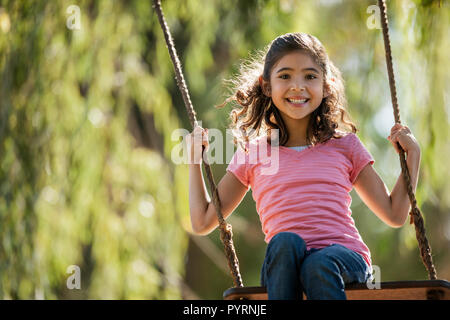 Lächelnden jungen Mädchen schaukeln auf eine Schaukel im Garten. Stockfoto