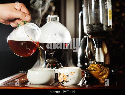 Die Hand eines Mannes gießt schwarzer Tee in eine schöne chinesische Schale Stockfoto