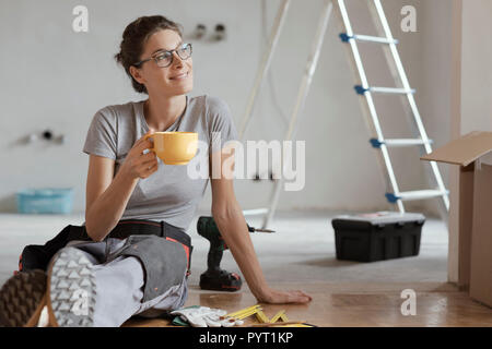 Junge lächelnde Frau mit einer Kaffeepause auf dem Boden und Weg suchen, sie tut ein Home Makeover Stockfoto