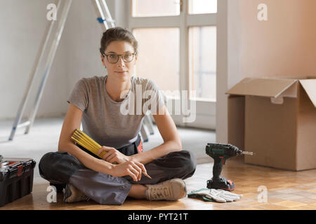 Junge Frau, die sich in ihrem neuen Zuhause und dabei eine Home Makeover, sie sitzt auf dem Boden mit Werkzeugen und Kartons Stockfoto