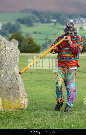 Neu - alter Mann bläst ein Didgeridoo in Richtung der Steine von Castlerigg Steinkreis im englischen Lake District, Cumbria, England Stockfoto