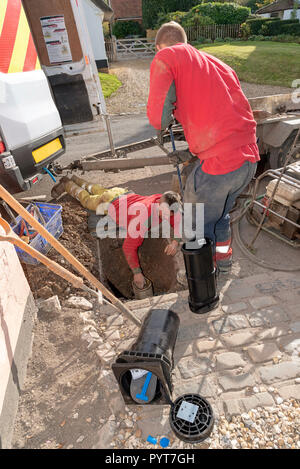 Installation einer neuen Wasseruhr in der Straße. UK. Mann lehnte sich in ein Loch, um die Installation zu machen Stockfoto