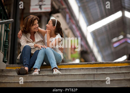Ältere Frau und ihre Enkelin mit ihren Armen um sich gegenseitig während an der Spitze der Treppe sitzen. Stockfoto