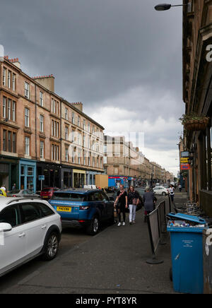 Eine vielbefahrene Straße in Glasgow, Schottland, mit Menschen zu Fuß die breite Bürgersteige und geparkten Autos am Straßenrand. Schottland. Stockfoto