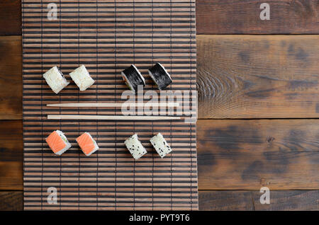 Sushi rollen und liegen auf einem hölzernen Eßstäbchen Bambus Stroh serwing Mat. Traditionelle asiatische Lebensmittel. Ansicht von oben. Stockfoto