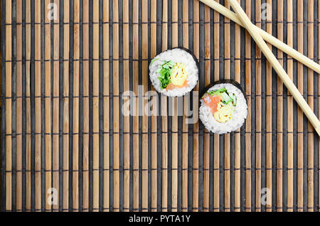 Sushi rollen und liegen auf einem hölzernen Eßstäbchen Bambus Stroh serwing Mat. Traditionelle asiatische Lebensmittel. Ansicht von oben. Flach Minimalismus shot mit kopieren. Stockfoto