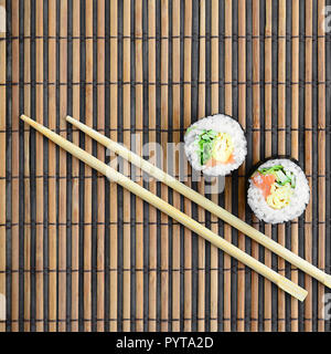 Sushi rollen und liegen auf einem hölzernen Eßstäbchen Bambus Stroh serwing Mat. Traditionelle asiatische Lebensmittel. Ansicht von oben. Flach Minimalismus shot mit kopieren. Stockfoto