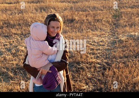 Schließen Sie eine junge Frau mit Baby genießt die Natur, Wandern und auf einem warmen Herbst sonniger Tag Chat im Hintergrund einer Feld- und Gelb sonnig. Mama's baby Stockfoto