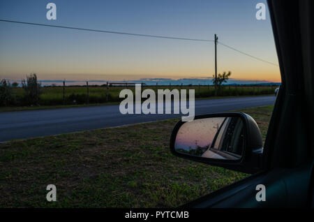 Straße von der Innenseite eines Autos und die Reflexion der Rückspiegel des Autos. Road Trip bei Sonnenuntergang, Sonnenuntergang aus dem Inneren des Autos. Stockfoto