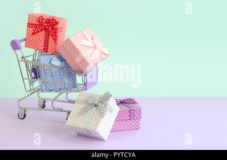 Kleines Geschenk Boxen in verschiedenen Farben mit Bändern liegt im Warenkorb auf ein Violett und Blau pastell Hintergrund. Stockfoto