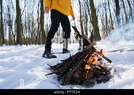 Junger Mann in gelber Jacke im Winter Wald in der Nähe von kleines Feuer. Stockfoto