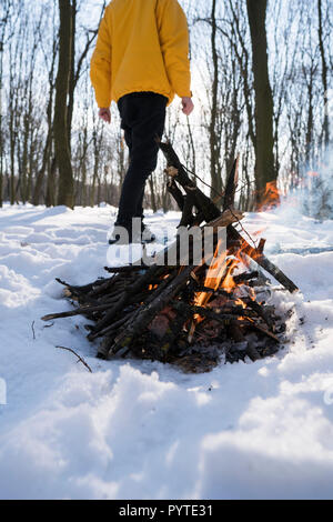 Junger Mann in gelber Jacke im Winter Wald in der Nähe von kleines Feuer. Stockfoto