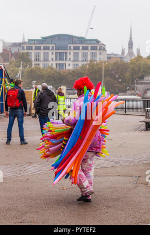 Eine hell gekleidete Mann in Rot Perücke Verkauf von Ballons auf dem South Bank in London, England, Großbritannien Stockfoto