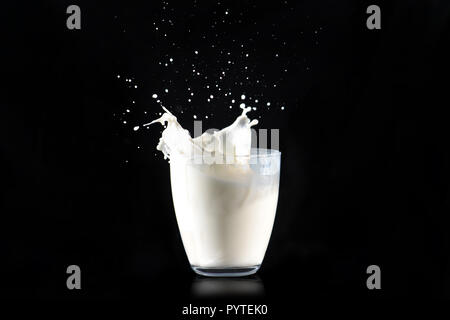 Spritzer Milch aus einem Glas transparent Glas auf einem schwarzen Hintergrund. Stockfoto