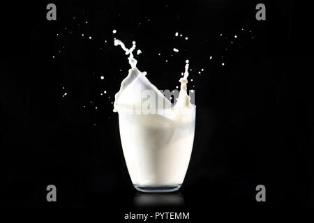 Einzigartige Milch spritzt aus einem Glas transparent Glas auf einem schwarzen Hintergrund. Stockfoto