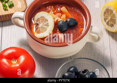 Suppe mit Fleisch saltwort, geräucherte Würstchen, Kartoffeln, Tomaten, Gurken, Zitrone mariniert, schwarzen Oliven und saure Sahne in Keramik Suppenteller mit Stockfoto