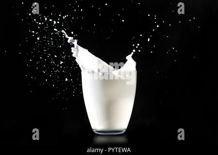 Spritzer Milch aus einem Glas transparent Glas auf einem schwarzen Hintergrund. Stockfoto