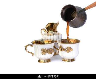 Kaffee fließt in eine weiße Tasse mit einem goldenen Griff und eine Blume. Zwei Tassen und ein Milchkännchen. Stockfoto
