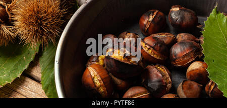 Gebratene Kastanien im Iron Skillet auf hölzernen Tisch. Stockfoto