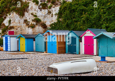 Bunten Badekabinen am Strand Bier in Devon, England mit einer umgestülpten Barke im Vordergrund. Stockfoto