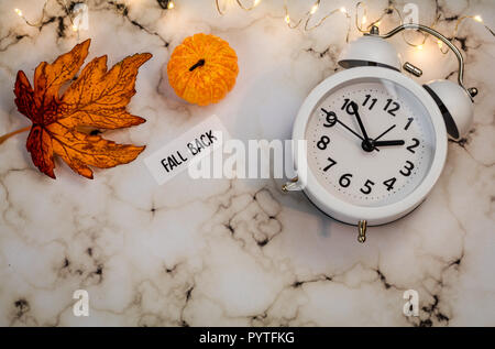 Zurück Sommerzeit Konzept mit weißen Wecker und Blätter im Herbst, flach auf Marmor legen Stockfoto