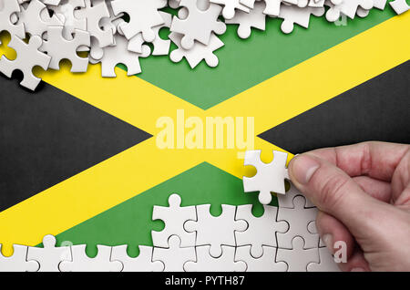Jamaika Fahne wird auf einen Tisch, auf dem die menschliche Hand ein Puzzle von weißer Farbe Falten dargestellt. Stockfoto