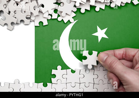 Pakistan Fahne wird auf einen Tisch, auf dem die menschliche Hand ein Puzzle von weißer Farbe Falten dargestellt. Stockfoto