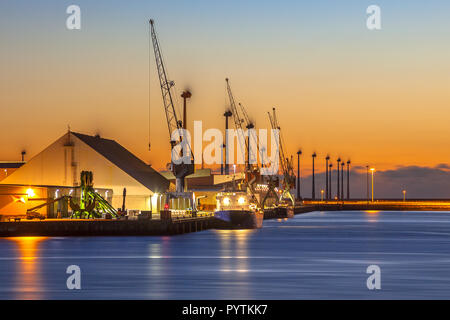 Boote auf einem Kai in einem kleinen Industriehafen während unter einem farbenfrohen Sonnenuntergang Stockfoto