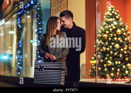 Ein junges Paar mit Paketen ist Einkaufen im Store gegenüber der Showcase am Weihnachtstag. Shopping im neuen Jahr. Stockfoto