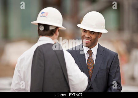 Zwei junge Ingenieure in einer geschäftlichen Besprechung beim tragen Anzüge und hardhats. Stockfoto