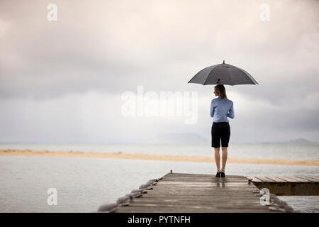 Geschäftsfrau Holding einen Regenschirm beim Stehen auf einem Bootsanleger. Stockfoto