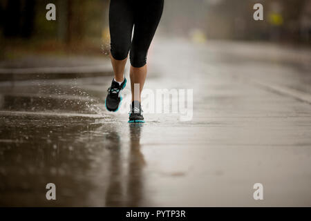 Junge Frau joggen auf einer Straße mit Wohnhäusern im Regen. Stockfoto