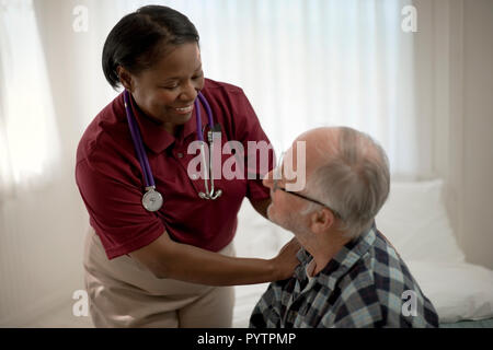 Gerne weibliche Krankenschwester beruhigend einen älteren Patienten an seinem Bett. Stockfoto