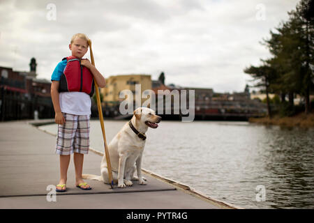 Nachdenkliche Junge warten auf einem Pier mit seinem Hund. Stockfoto