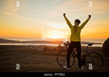 Junge Frau, die ihre Arme sich heben in Sieg nach dem Radfahren auf der Spitze eines Hügels. Stockfoto