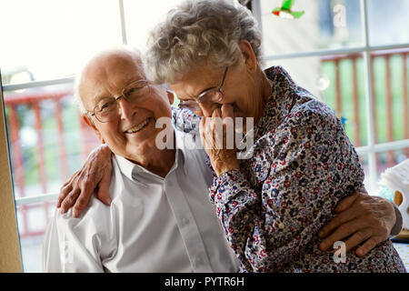 Liebevolle ältere Paare teilen sich ein Lachen, während Sie in der Küche Fenster setzen sich zusammen. Stockfoto