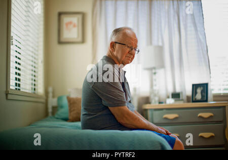 Einsame ältere Mann auf seinem Bett in einem Altersheim sitzen. Stockfoto