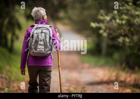 Reife Frau geht für eine Wanderung auf einem grünen Wald Trail. Stockfoto