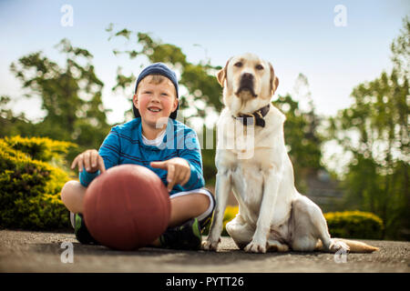 Lächelnde junge Junge sitzt mit seinem Hund. Stockfoto