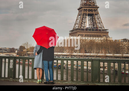 Herbst in Paris, Paar unter roten Regenschirm in der Nähe von Eiffelturm, Herbst, Liebe in regnerischen Tag, romantischen Moment auf der Brücke Stockfoto