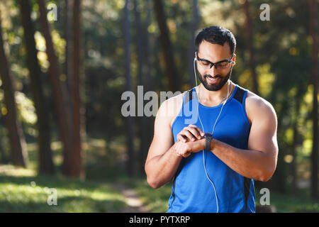 Junge athletische multikulturellen bärtigen Mann mit sportish Gläser, die Pause nach dem Joggen, Musik hören und auf seine sportish beobachten, gesunden Lebensstil und Personen Konzept Stockfoto