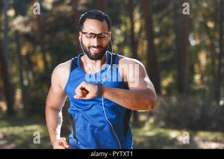 Junge athletische multikulturellen bärtigen Mann mit Brille auf dem sportish sportish sehen und hören seine Lieblingsmusik beim Joggen, gesunden Lebensstil und Personen Konzept Stockfoto