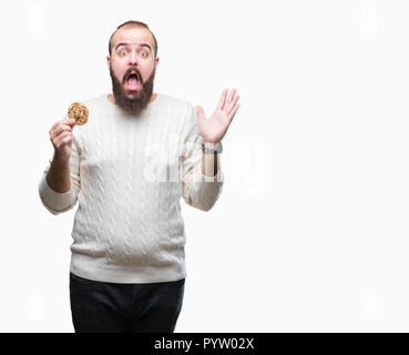 Junge hipster Mann essen Chocolate Chips Cookies über isolierte Hintergrund sehr glücklich und aufgeregt, Sieger Ausdruck feiern Sieg mit schreienden Stockfoto