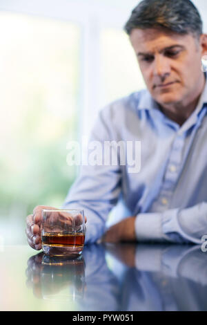 Unglücklich reifer Mann mit Alkohol Problem Holding Glas Whiskey zu Hause Stockfoto