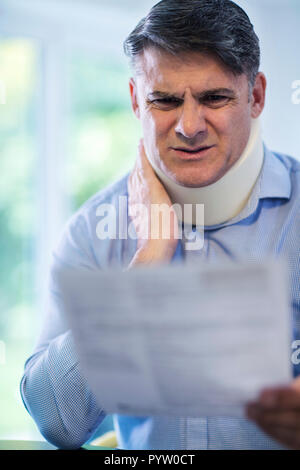 Reifer Mann Lesen Schreiben nach Erhalt die Nackenschmerzen Stockfoto