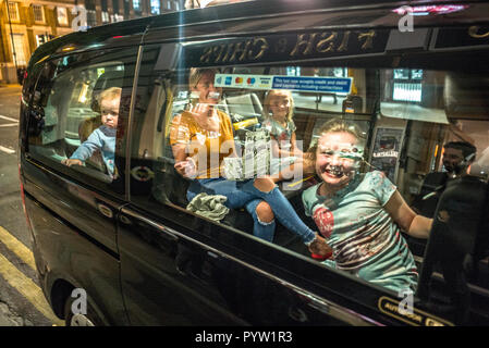 Familie im Taxi vor dem Fish and Chips Shop London. Mutter und drei Kinder im Auto, die vor der Kamera lächelten. Ein Kind sieht unglücklich aus Stockfoto